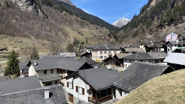 A mountain village with traditional buildings, a valley, and a snow-capped peak in the background. - Della Posta Stambecco by Interhome (Rossa)
