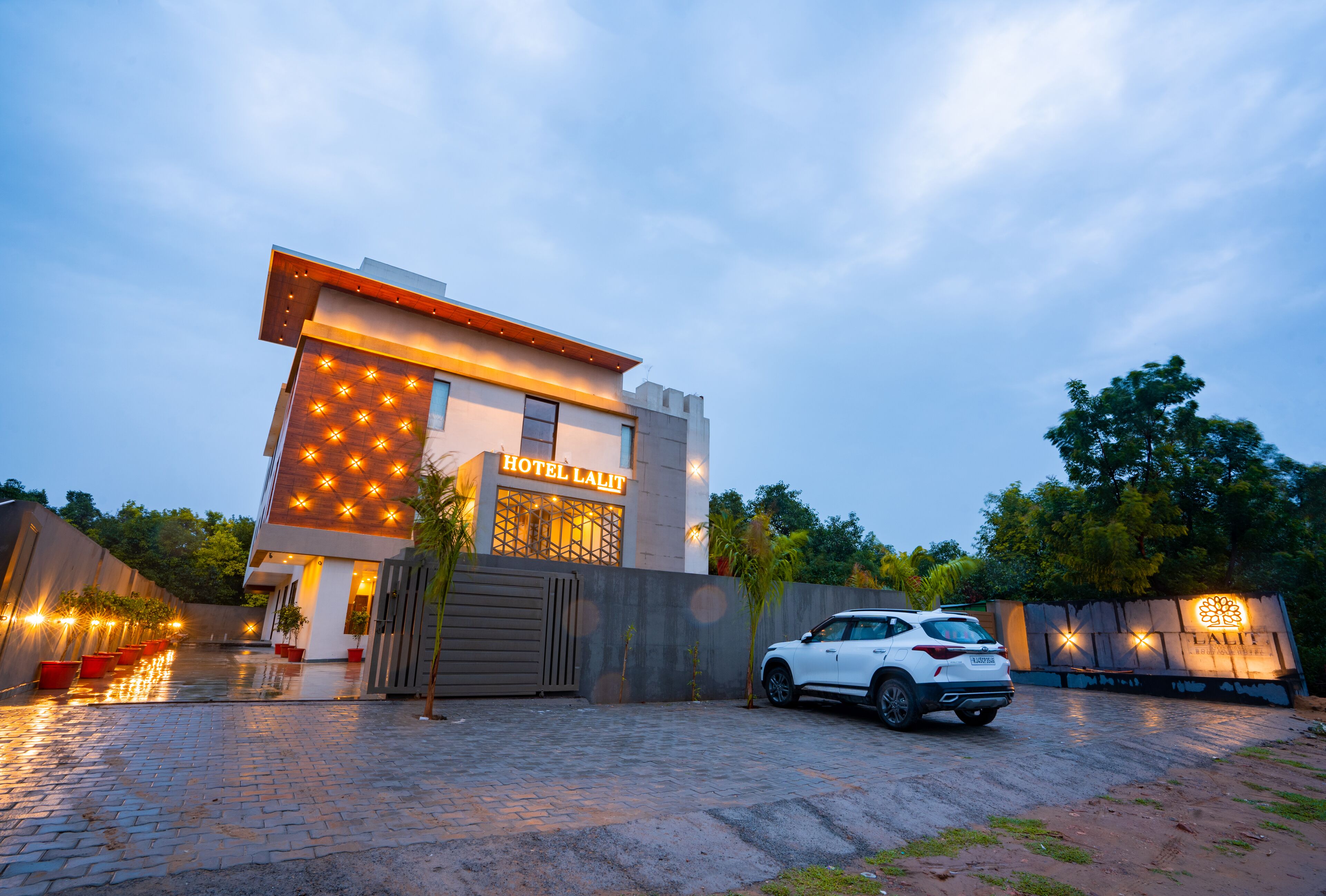 A modern hotel with a prominent sign, a paved driveway, and a parked car.