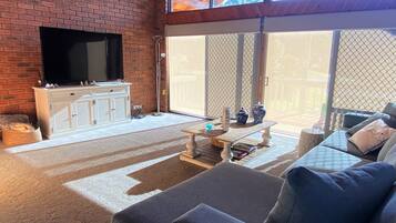 A living room with a brick fireplace, a flat-screen TV, a white cabinet, and a large sliding glass door leading to an outdoor area.