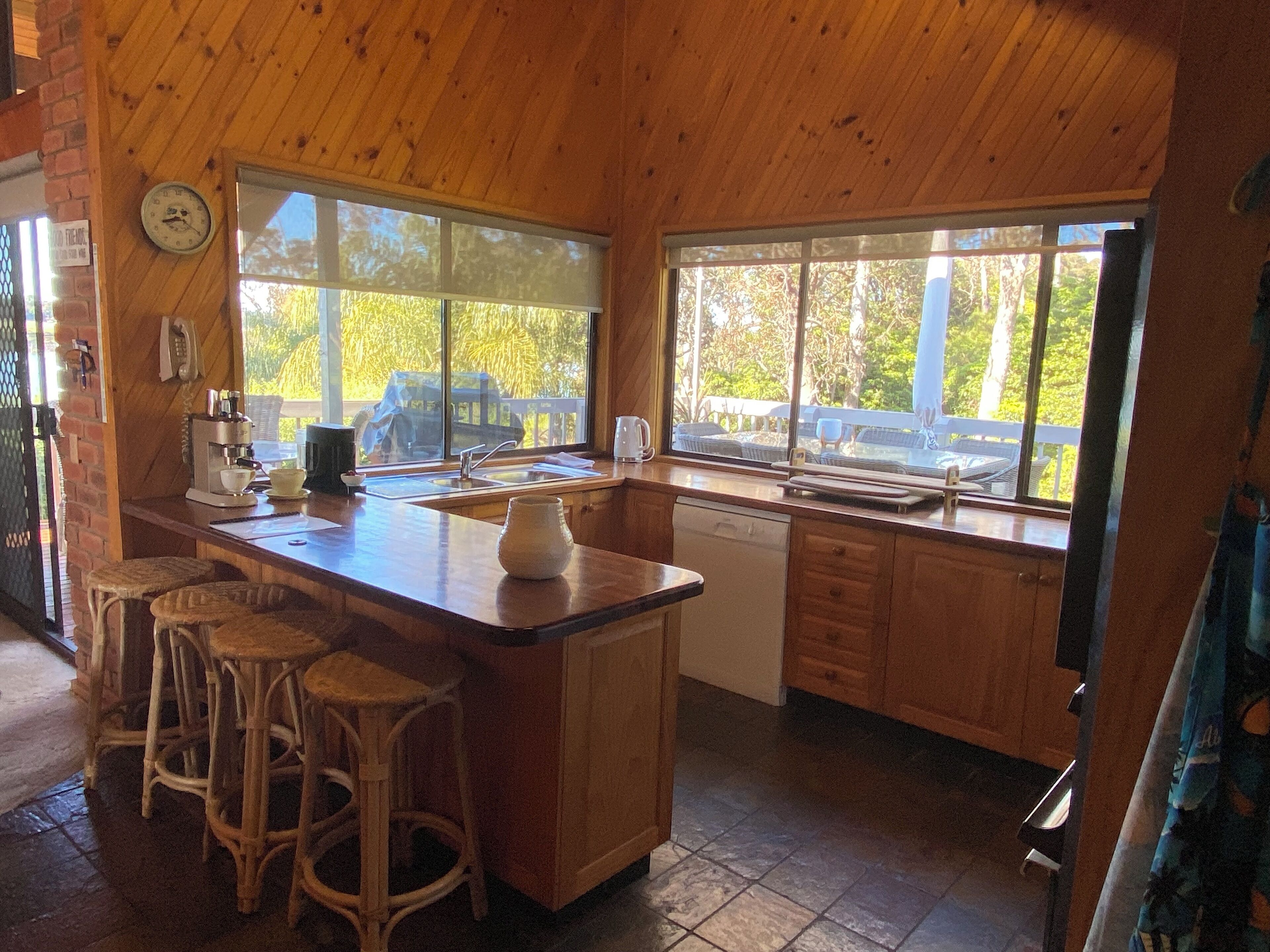 A wooden kitchen with a large island, bar stools, a coffee machine, and a view of the outdoors.