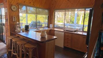 A wooden kitchen with a large island, bar stools, a coffee machine, and a view of the outdoors.