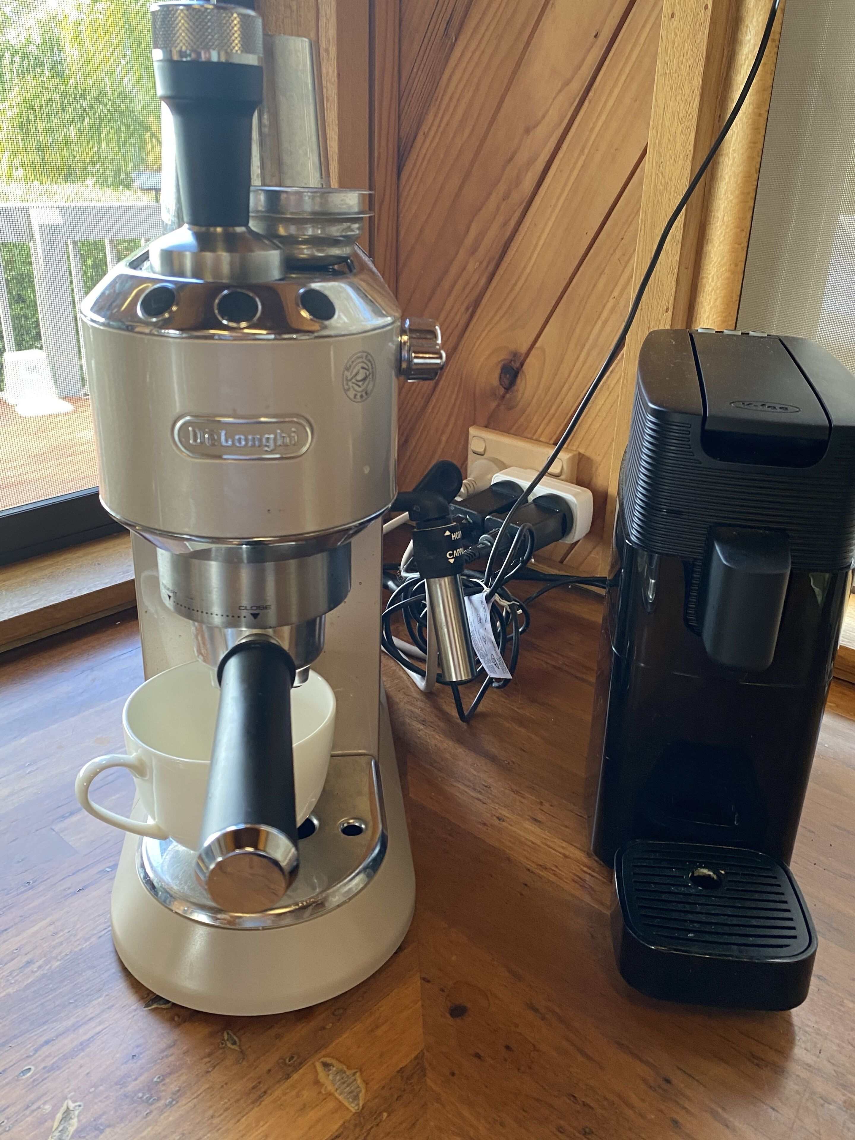 Máquina de café com suporte para xícara e cafeteira em mesa de madeira.