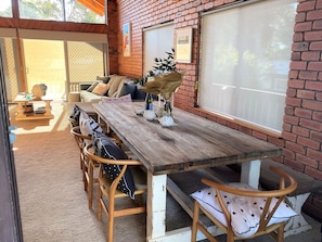 Ein gemütlicher Essbereich im Freien mit einem Holztisch und Korbstühlen, einer Ziegelwand und einer Glastür zum Patio.