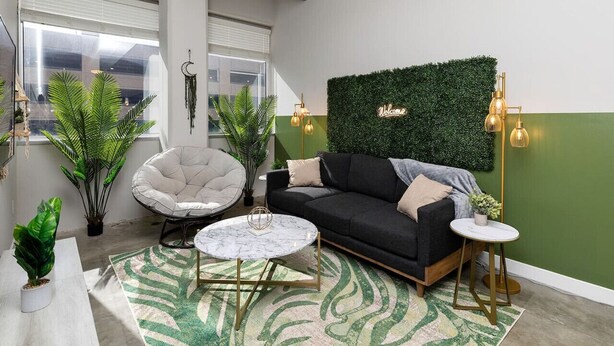 Una sala de estar moderna con un sofá negro, una mesa de centro redonda y una pared verde con un letrero que dice 'Welcome'.