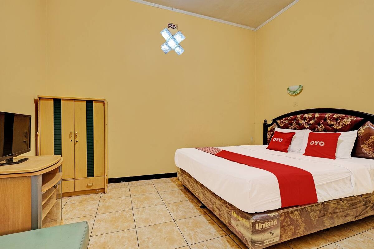 A bedroom with a bed, a TV, a wardrobe, and a small table.