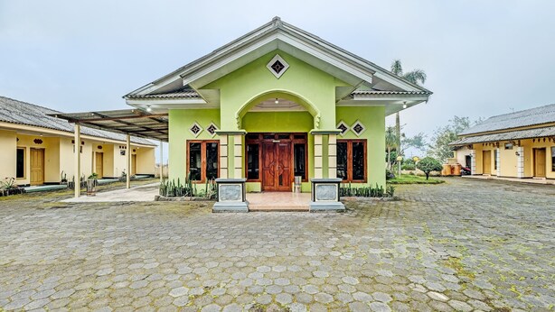 A building with a green facade, a central entrance with a wooden door, and a tiled courtyard. - OYO 92406 Hotel Renata 1 (Getasan)