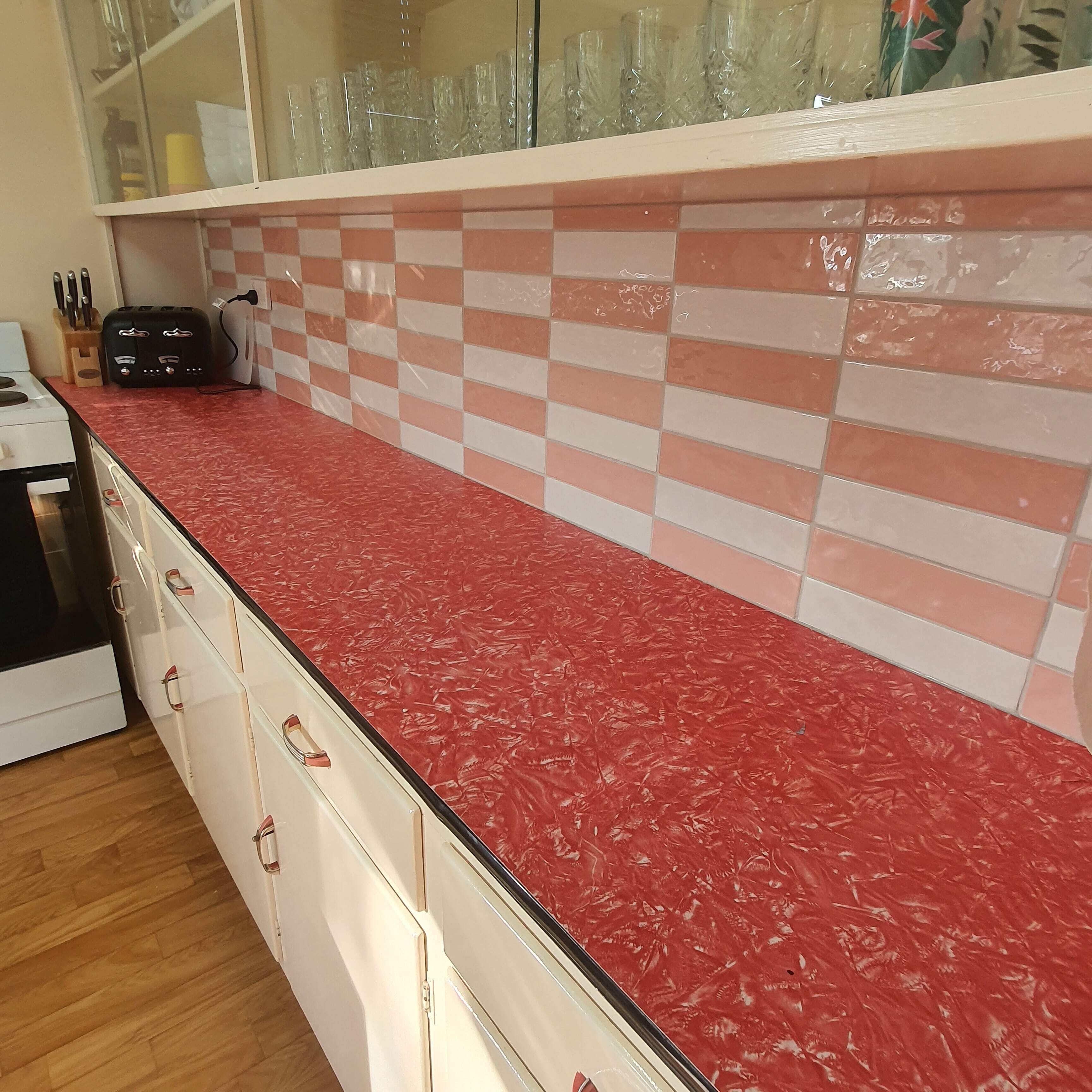 A kitchen with a red countertop, white cabinets, and a checkered backsplash.