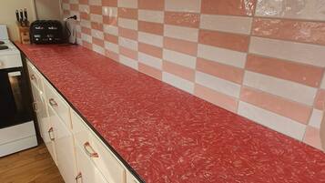A kitchen with a red countertop, white cabinets, and a checkered backsplash.