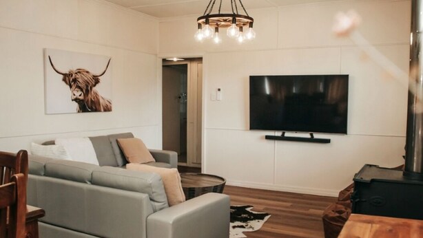 A modern living room with a grey sofa, a wooden coffee table, a flat-screen TV mounted on the wall, and a ceiling light fixture.