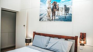 A bedroom with a bed, a nightstand, a wall-mounted lamp, and a painting of horses.