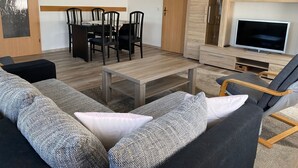 Ein modernes Wohnzimmer mit Holzesstisch und -stühlen, einer Sofagarnitur, einem Fernseher und einem Holzschrank.