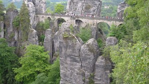 Eine Steinbrücke, die Felsformationen mit einem bewaldeten Tal im Hintergrund verbindet.