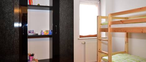 A room with a bunk bed, a black bookshelf, and a window with a white curtain.