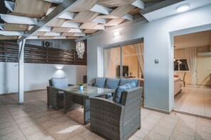 A modern living area with a glass-top table, wicker furniture, and a ceiling with geometric wooden panels.