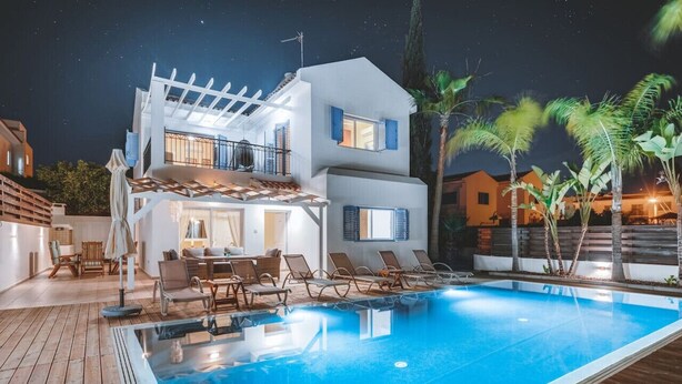 Ett modernt hus i två våningar med en swimmingpool, en uteplats och en pergola.
