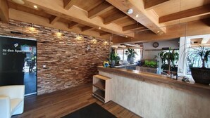 A reception area with a stone wall, wooden ceiling beams, a reception desk, and potted plants.