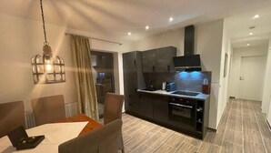 A modern kitchen with dark cabinets, a built-in oven, and a microwave. There is a dining area with a table and chairs.