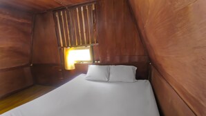 A single bed with white bedding in a wooden room with a slanted ceiling.