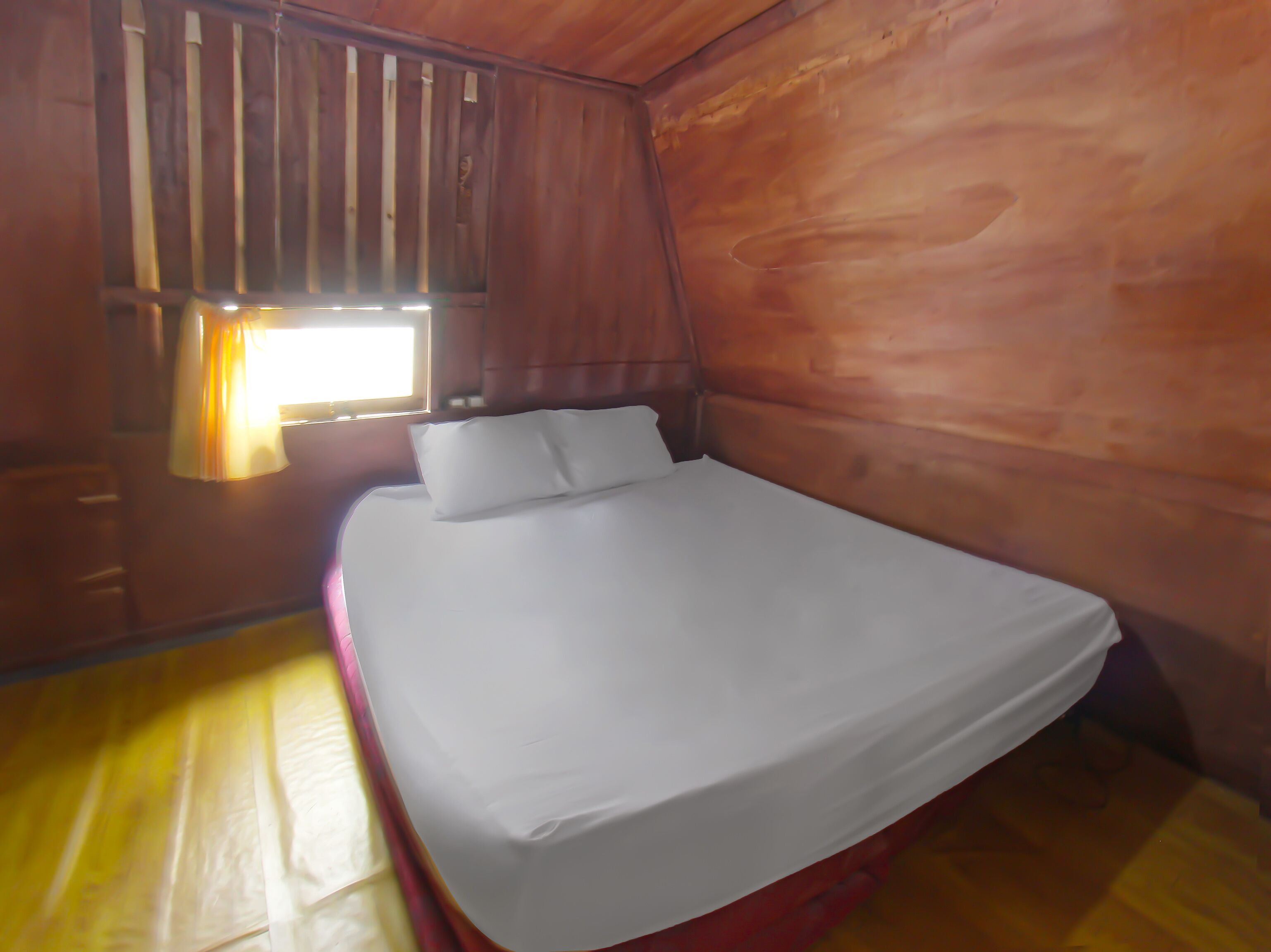 A single bed with white bedding in a room with wooden walls and a window with blinds.