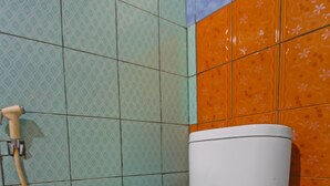 A toilet with a white tank and seat, set against a wall with patterned tiles in green, orange, and blue.