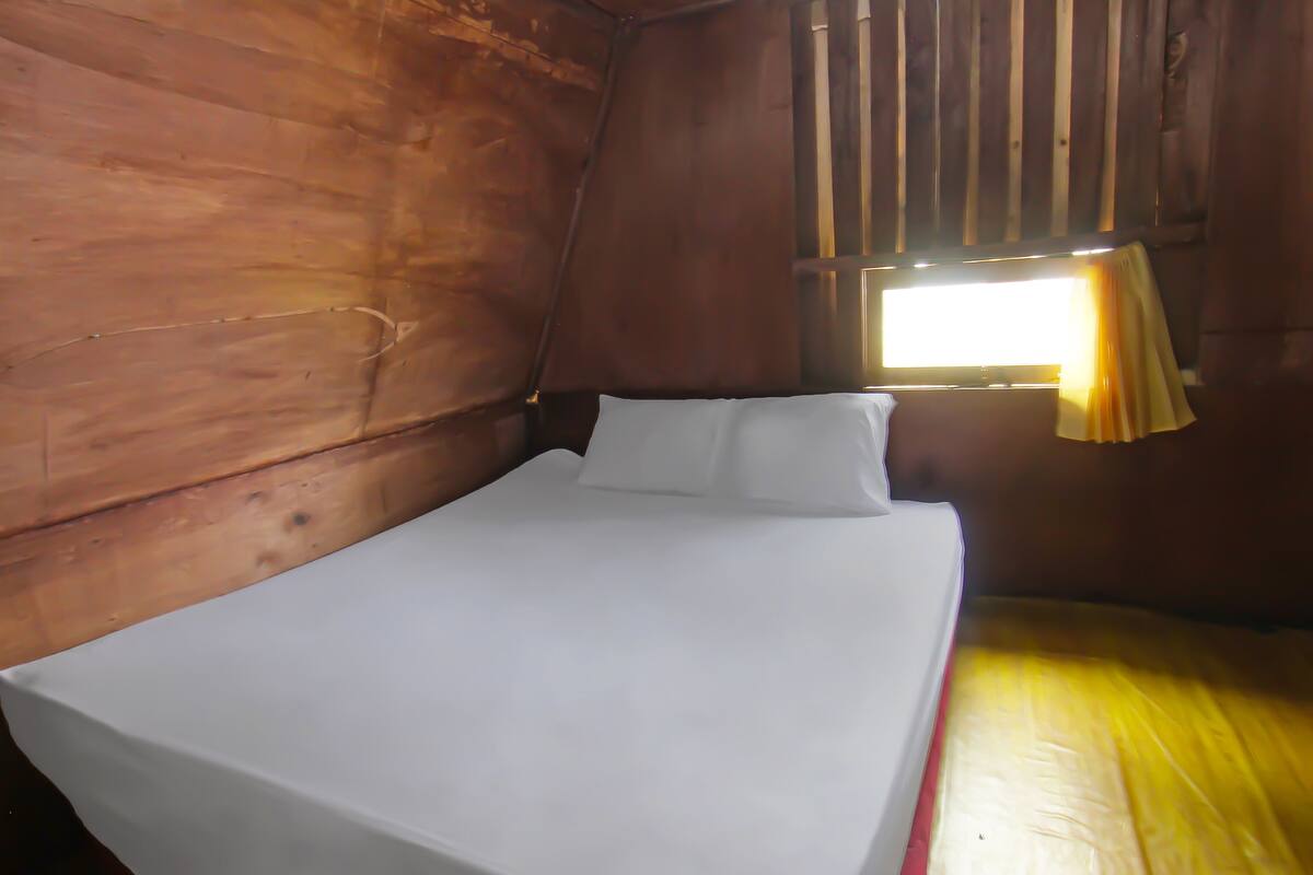 Un lit simple dans une chambre en bois, avec une fenêtre et des rideaux.