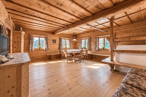 A wooden cabin interior with a dining table, chairs, a bench, and a television on the left. - Chalet Ulten (Santa Valburga)