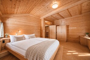 Une chambre dans une cabane en bois, avec un lit, des tables de chevet, une armoire et une petite table de nuit.