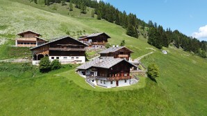 Eine Gruppe aus Holzgebäuden an einem Hang mit freiem Blick auf den umliegenden Wald.