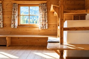 Interior de una cabaña con un banco de madera, una ventana con cortinas y una cama literera.