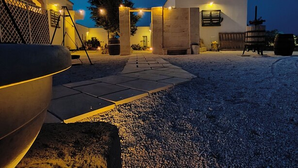 A modern outdoor patio area with a stone floor, a large bowl, and a small building with a chimney. - MASSERIA TENUTA SOFIA (Otranto)