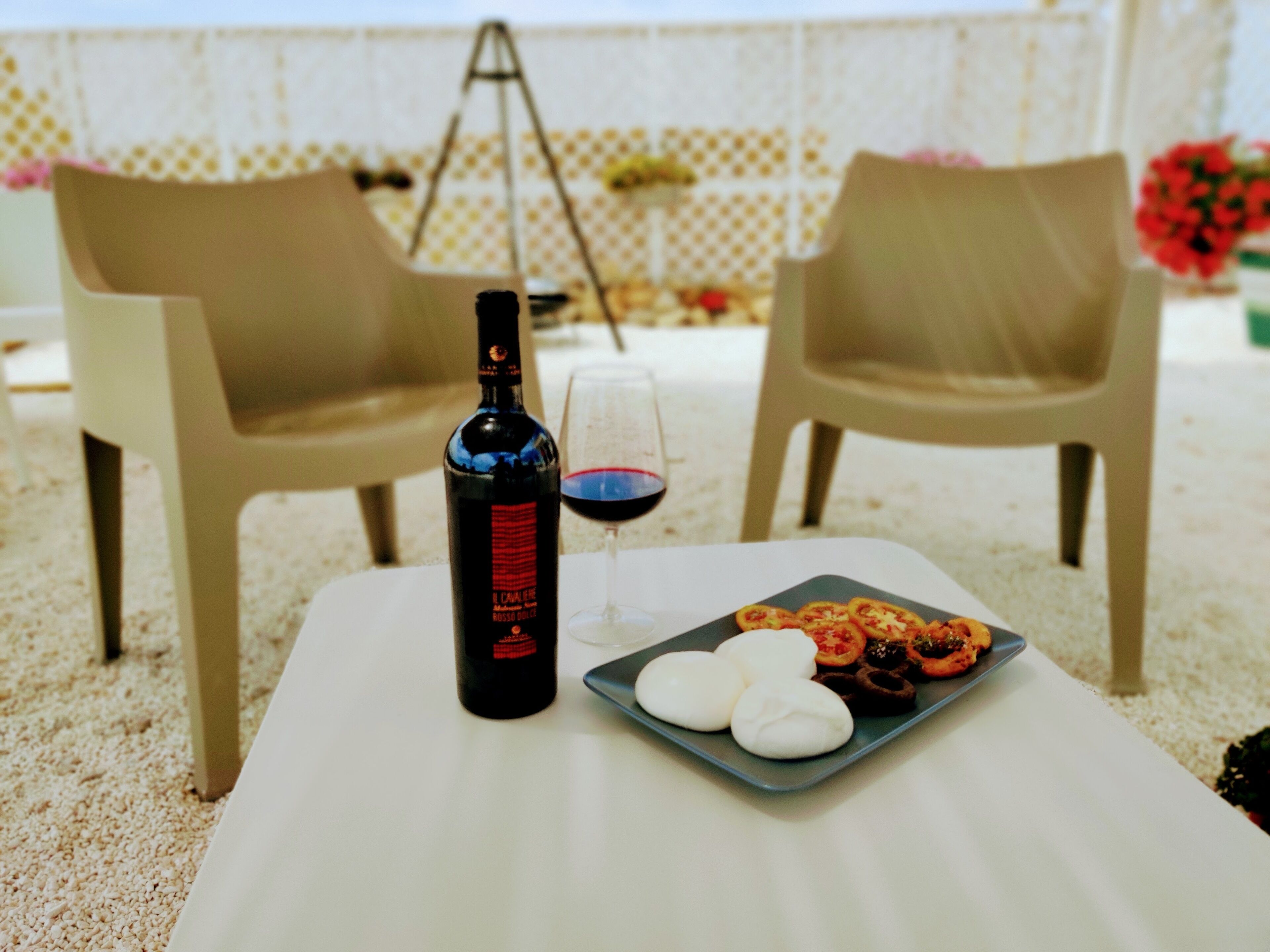 A table with a bottle of rosé wine, a glass of wine, and a plate of food including bread and tomatoes.