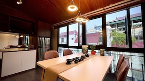 A modern kitchen with wooden ceiling, large windows, and a dining table set with bowls and a plant. - Maison Mackeno (Hanoi)