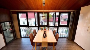 A dining area with a wooden ceiling, large windows, a table with chairs, and a refrigerator. - Maison Mackeno (Hanoi)