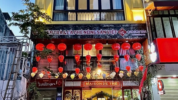 A building with multiple stories, featuring a ground-level storefront with a sign that reads "MAISON DE THE". There are several motorcycles parked in front, and the entrance is decorated with red lanterns. - Maison Mackeno (Hanoi)