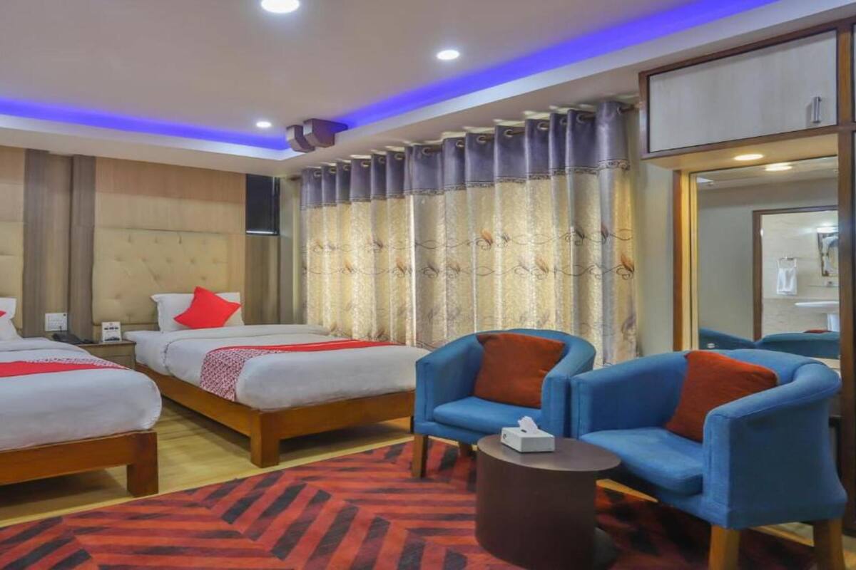 Een hotelkamer met twee bedden, een blauwe fauteuil, een klein rond tafeltje en een grote spiegel.
