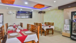 Un espace repas avec des tables disposées pour accueillir quatre personnes, un téléviseur fixé au mur et un distributeur de boissons.