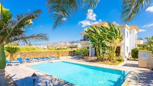 A swimming pool with lounge chairs, palm trees, and a building with balconies. - Villa Dora in Argaka (Argaka)