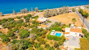 An aerial view of a coastal property with a swimming pool, multiple buildings, and a road leading to the beach.
