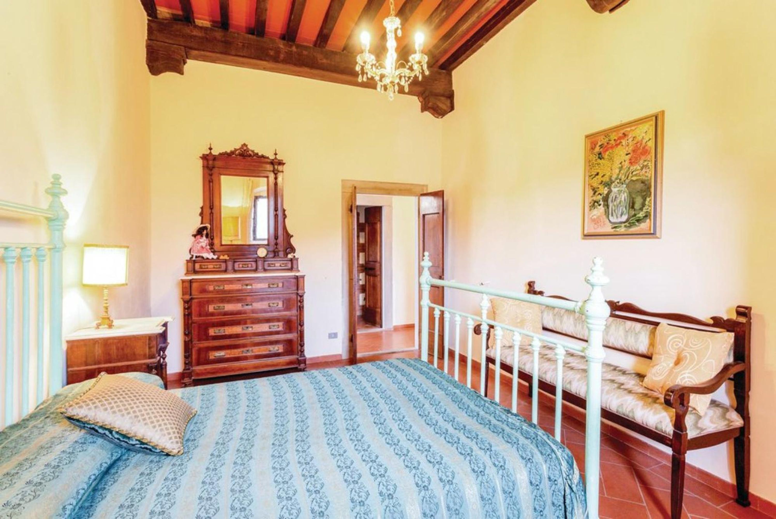 A bedroom with a bed, dresser, mirror, and a bench with cushions.