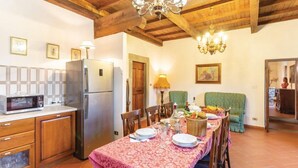 Une cuisine avec des poutres en bois, un réfrigérateur, un four à micro-ondes et une table à manger dressée avec des assiettes et un panier de fruits.