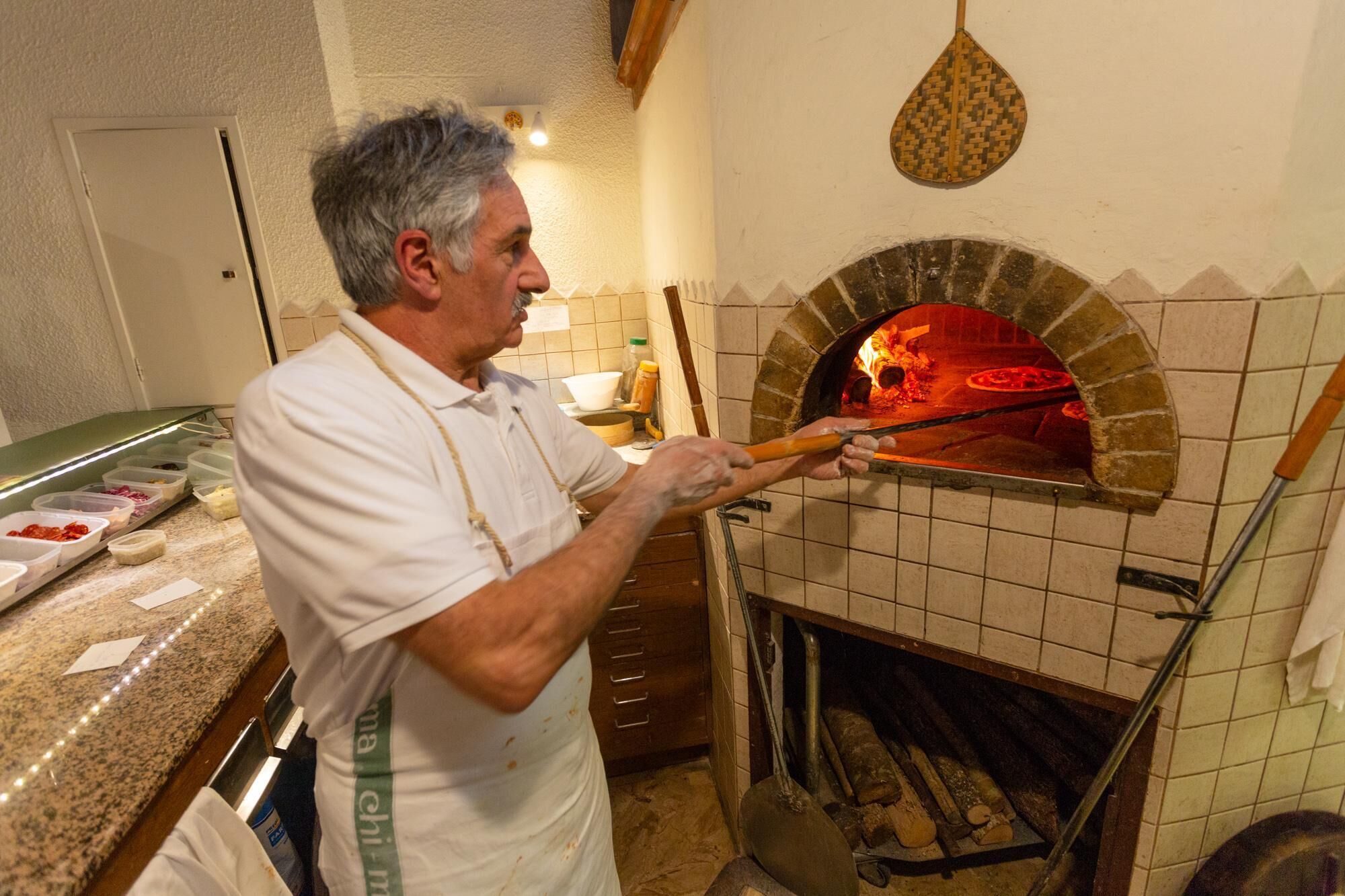 A person using a long-handled tool to manage a pizza in a brick oven.