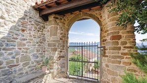Un arc en pierre mène à une entrée fermée par un portail, d’où l’on peut admirer un paysage montagneux.