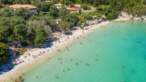 An aerial view of a beach with people swimming and sunbathing, surrounded by trees and buildings. - Lakka Bay View Collection (Paxos)
