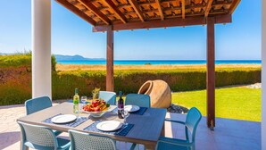 An outdoor dining area with a table set for two, overlooking a beach and ocean. - Blue Bay Villas Collection (Polis)