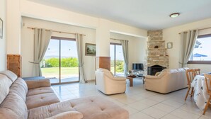 A spacious living room with a beige sofa, a fireplace, and a dining area with a table and chairs. - Blue Bay Villas Collection (Polis)