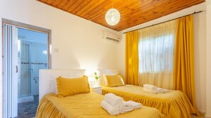 Een hotelkamer met twee bedden, een houten plafond, een airconditioning en een schuifdeur naar een douchegedeelte.