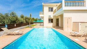 A swimming pool with lounge chairs, a building with balconies, and a clear sky. - Rose Villas Collection (Ayia Marina Chrysochous)
