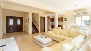 A spacious living room with a beige sofa, a white coffee table, and a staircase leading to another level. - Rose Villas Collection (Ayia Marina Chrysochous)