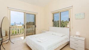 A bedroom with a bed, a nightstand, a mirror, and a balcony with a view. - Rose Villas Collection (Ayia Marina Chrysochous)
