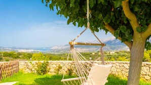 Una silla hamaca colgada de un árbol, con vistas a un paisaje de montañas y un muro de piedra.
